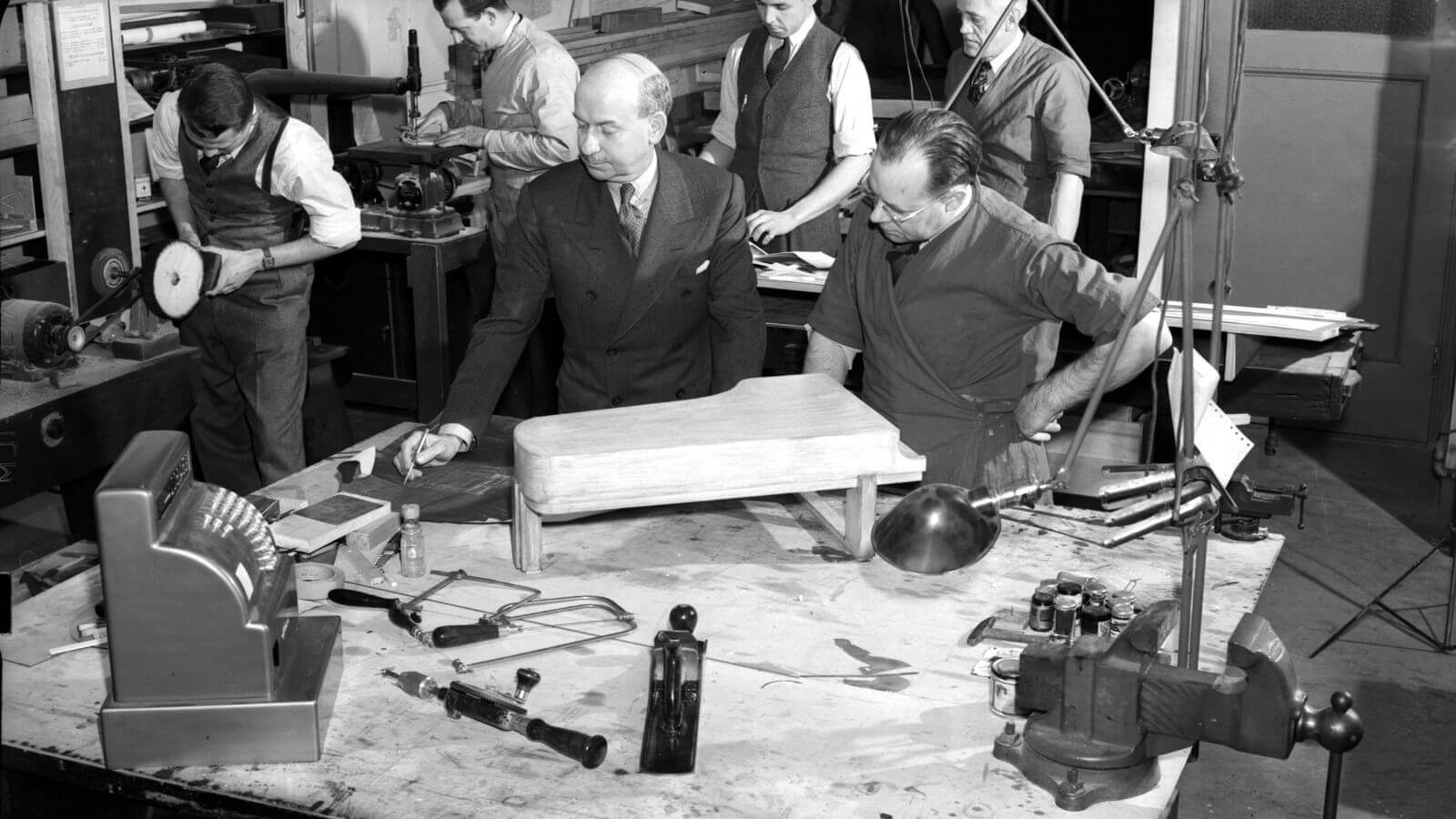 Black and white photo of individuals working on prototype of piano